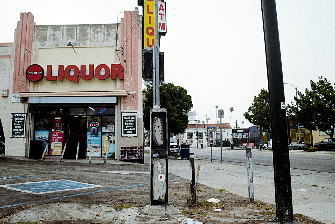 "Street photography of a graffiti-tagged payphone in front liquor store, urban decay scene in Los Angeles."