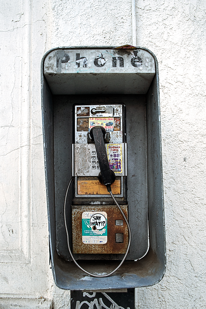 Urban decay street photography of an abandoned payphone against a white wall in Los Angeles.